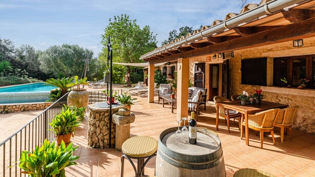 Une terrasse extérieure avec une piscine, des piliers en pierre, des meubles en osier et une bouteille de vin.