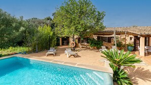 Une piscine avec des chaises longues, un arbre et un bâtiment doté d’un toit en tuiles.