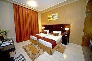Une chambre d’hôtel avec deux lits, un bureau, une chaise et une grande fenêtre avec des rideaux.