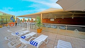 A rooftop terrace with sun loungers, a covered seating area, and a view of the cityscape. - Two Bedroom Apartment Near NMC Sociality Hospital (Dubai)