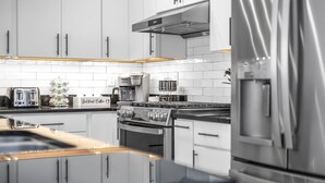 A modern kitchen with white cabinets, stainless steel appliances, and a wooden countertop.