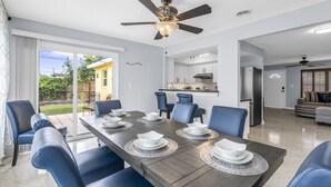 A modern dining room with a long table set for six, blue chairs, and a ceiling fan.