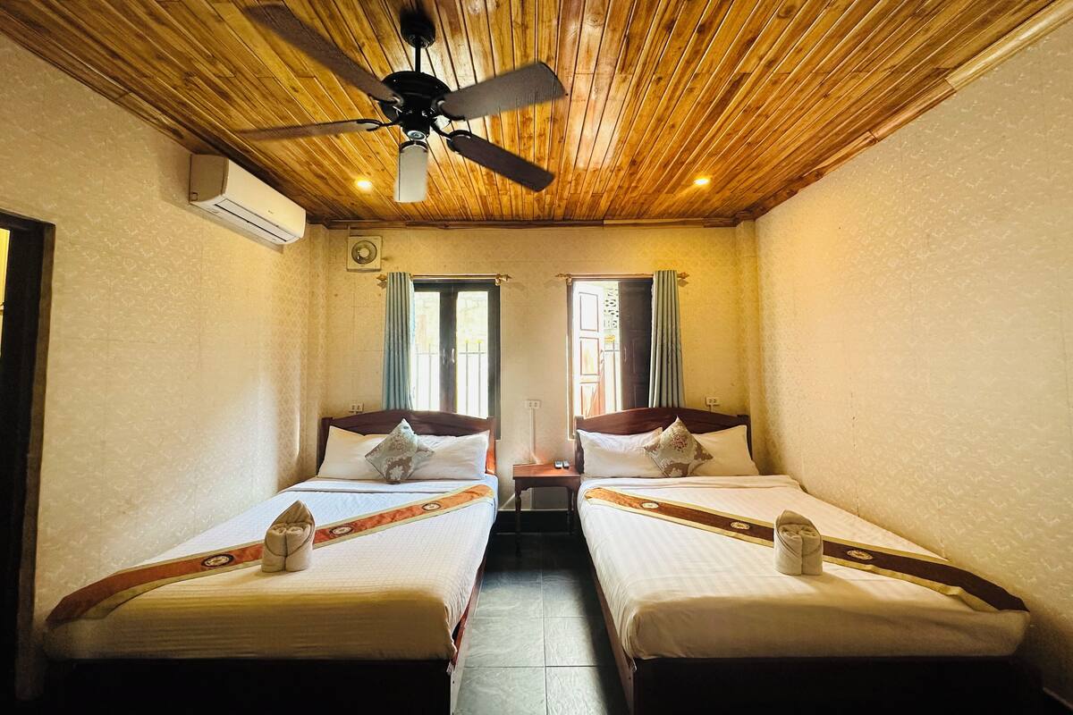 A room with two beds, a ceiling fan, and a window with curtains.