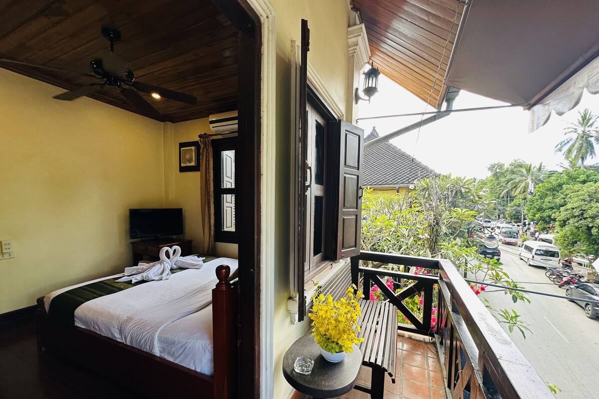 A hotel room with a bed, a TV, and a balcony with a table and flowers.