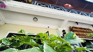 A hotel entrance with a signboard, large green plants in the foreground, and a balcony with railings. - Anisa Mekong Riverside Villa (Luang Prabang)