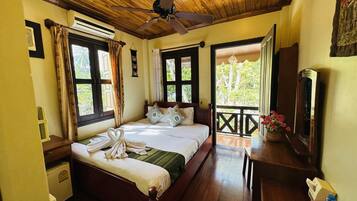 Un dormitorio con techo de madera, una cama con manta verde, una mesita de noche de madera, un aparador, un espejo y una ventana con cortinas.