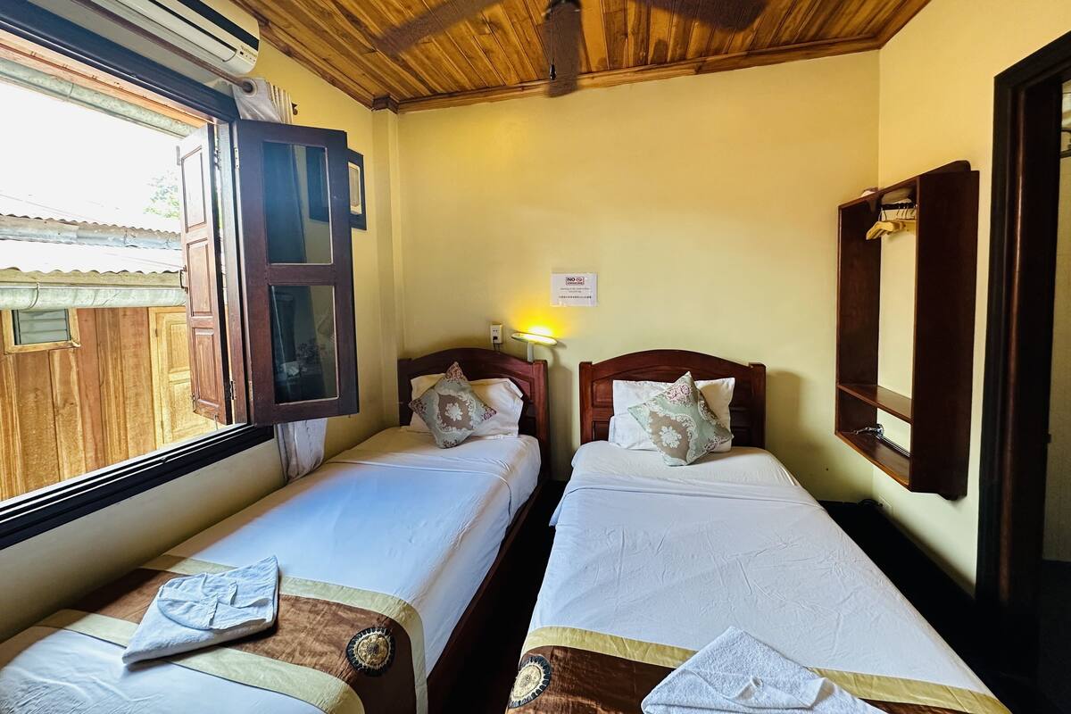 A room with two single beds, wooden ceiling, a window, and a mirror.