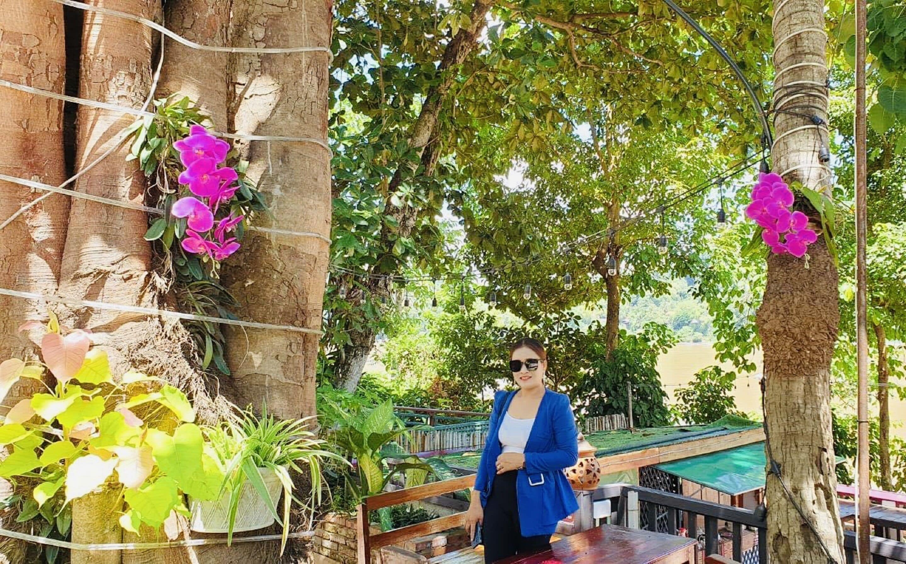 A woman standing on a wooden deck with a view of a pool and lush greenery.