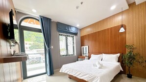 A modern hotel room with a large bed, a wooden accent wall, a potted plant, and a balcony with a view. - Milanesa Hotel & Apartment (Ho Chi Minh City)