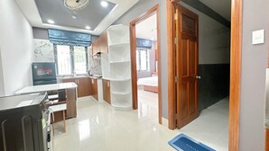 A modern kitchen with a refrigerator, a microwave, and a sink. There is a dining table with chairs. The room has a ceiling fan and a window with curtains. - Milanesa Hotel & Apartment (Ho Chi Minh City)