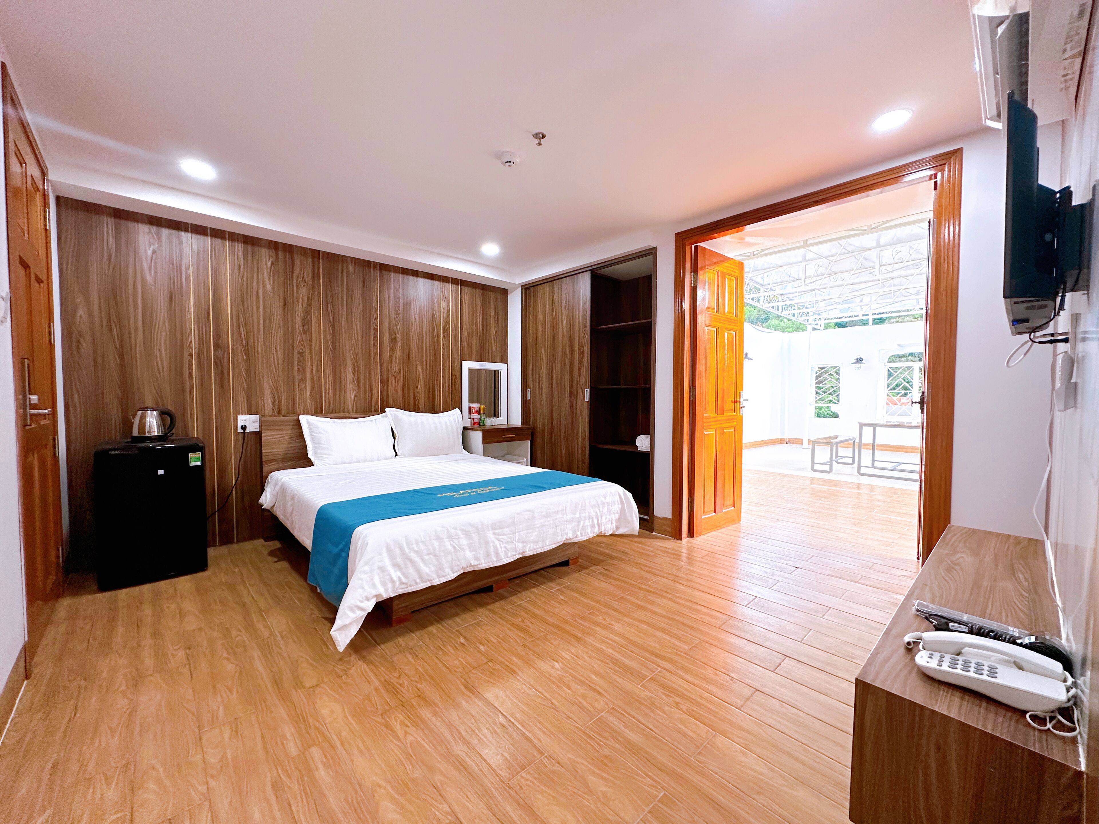 Une chambre d’hôtel avec un plancher en bois, un lit recouvert d’une courtepointe bleue et blanche, un petit bureau avec un téléphone et une armoire.