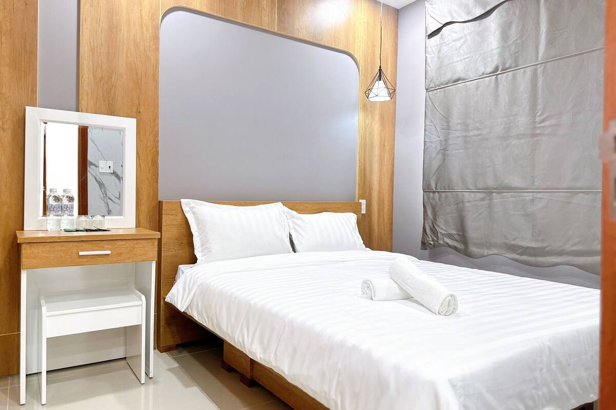 A neatly made bed with white linens, a wooden headboard, and a bedside table with a mirror and water bottles.
