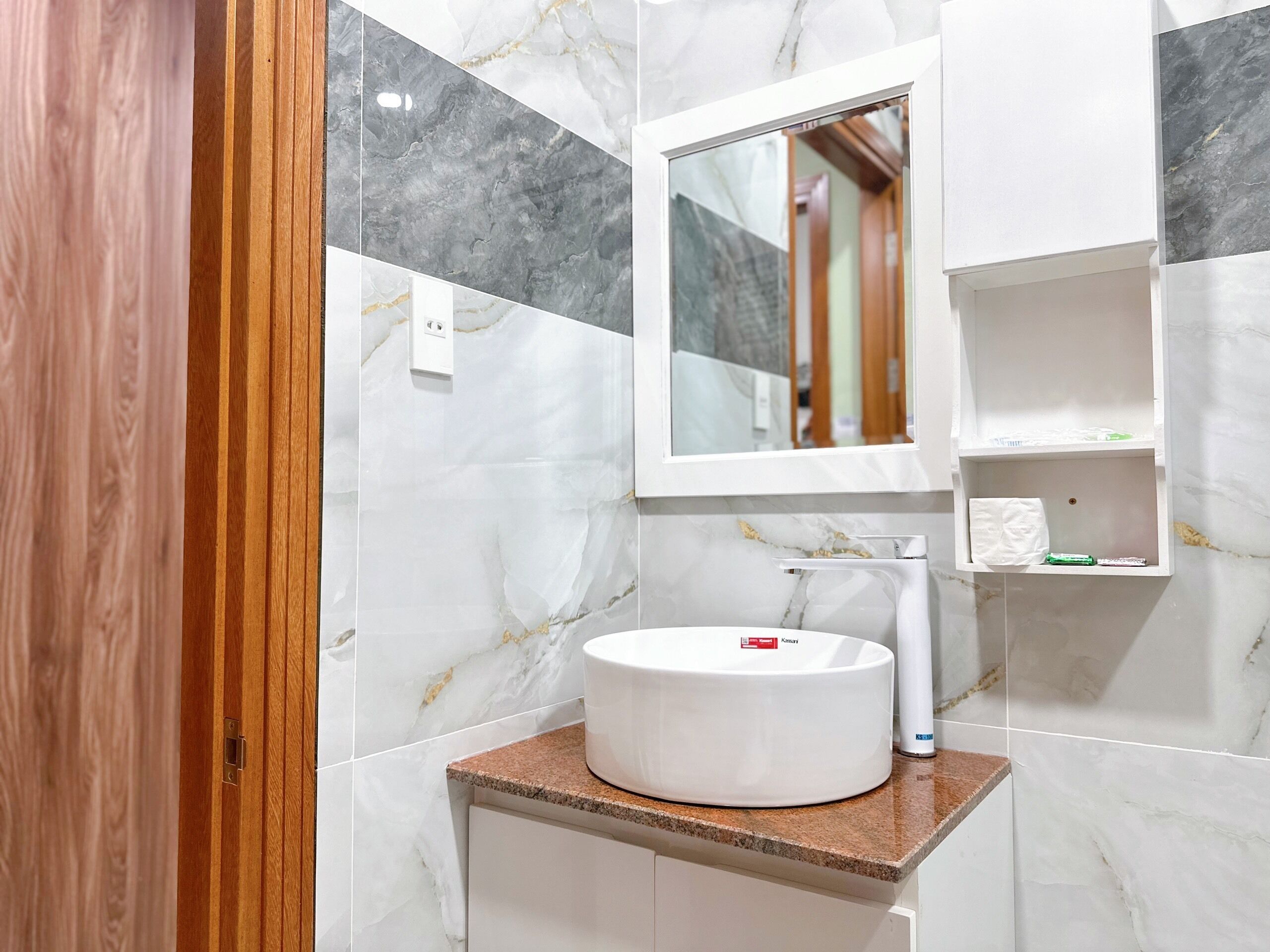 Un bagno con parete in marmo, un lavabo tondo, uno specchio e un appendi asciugamani.