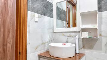 Un bagno con parete in marmo, un lavabo tondo, uno specchio e un appendi asciugamani.