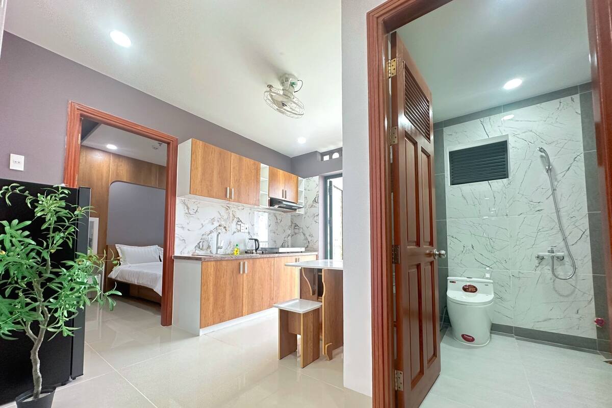 A modern hotel room with a kitchenette, a shower area, and a potted plant.