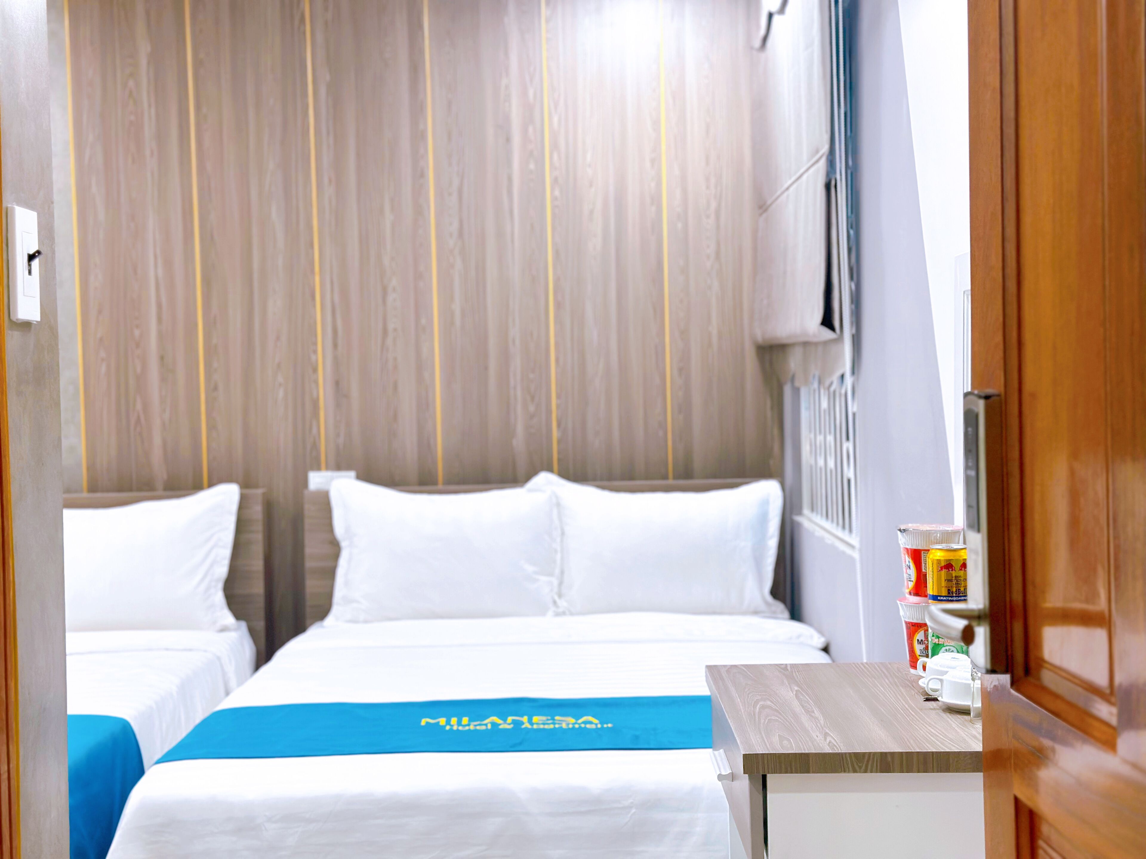 A hotel room with two beds, a wooden headboard, a small table with toiletries, and a blue towel on the bed.
