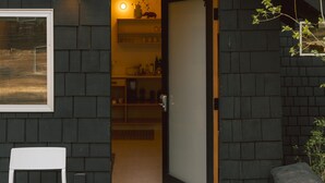 Ein Gebäude mit dunkler Fassade, ein Fenster mit weißem Rahmen und eine Tür zu einem Innenraum.
