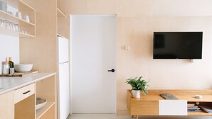 Eine moderne Küche mit Holzausstattung, einer weißen Tür, einem flachbildfernseher an der Wand und einem Holzessttisch mit Topfpflanze.