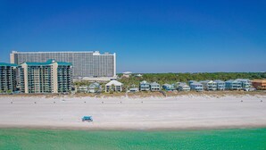 Ein Strandhotel mit mehreren Gebäuden, darunter ein großes Resort und kleinere Häuser, an einem Sandstrand mit klarem türkisblauem Wasser.