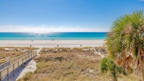A beach with a wooden walkway leading to the shore, clear blue sky, and ocean.