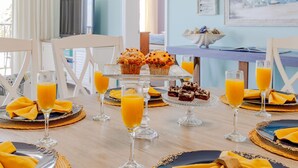 A breakfast setting with a table set for four, featuring orange juice glasses, muffins, and a dessert tray.