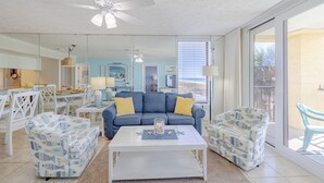 A spacious living room with a blue sofa, white armchairs, and a coffee table.