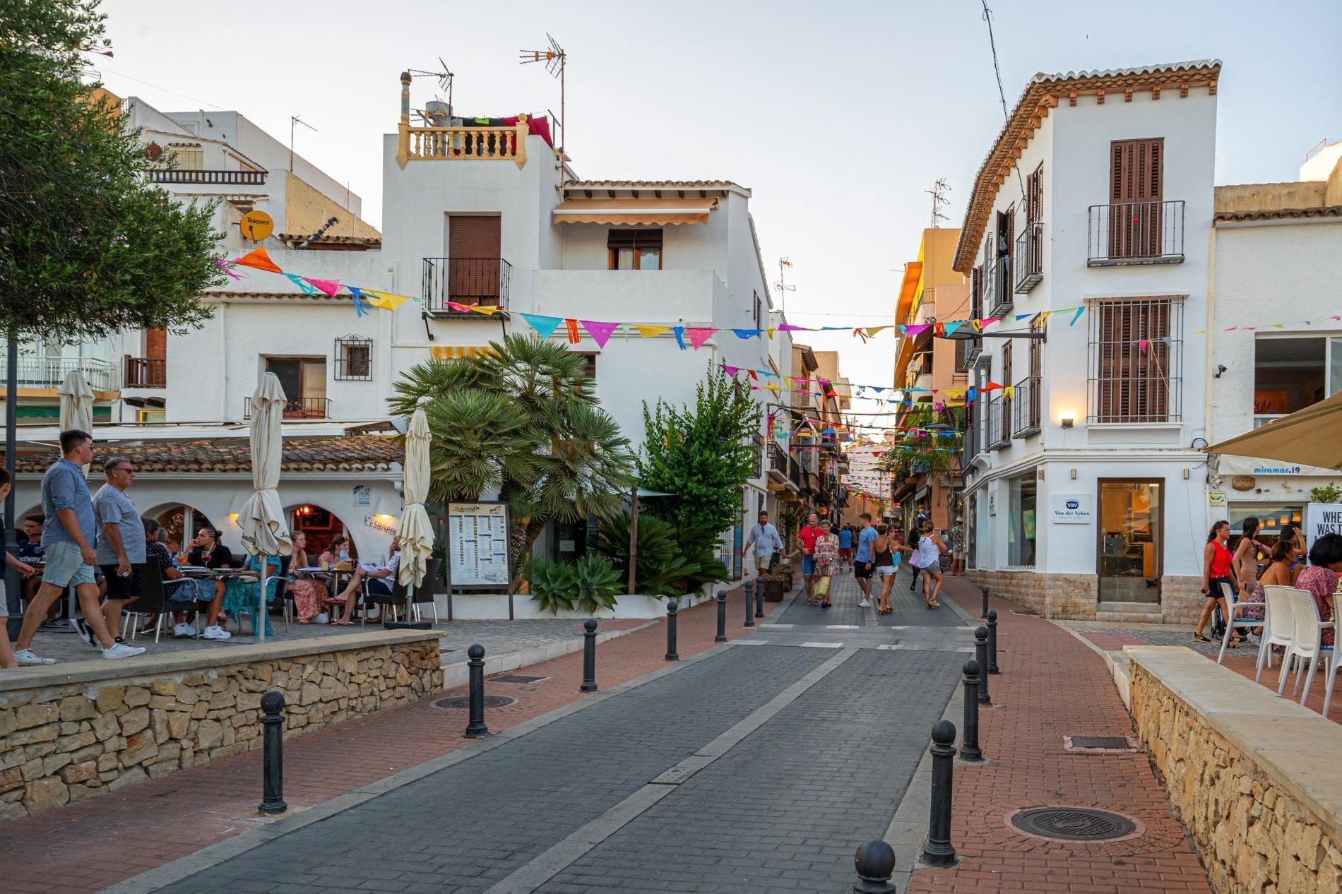A narrow street lined with buildings, some with balconies and outdoor seating areas.