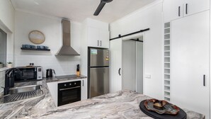 A modern kitchen with white cabinetry, a stainless steel refrigerator, a built-in oven, a microwave, and a clock on the wall.