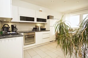 A modern kitchen with white cabinets, a built-in oven, a coffee maker, and a refrigerator.