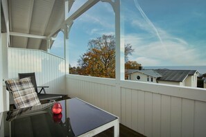 A covered balcony with a table, chair, and a red vase.