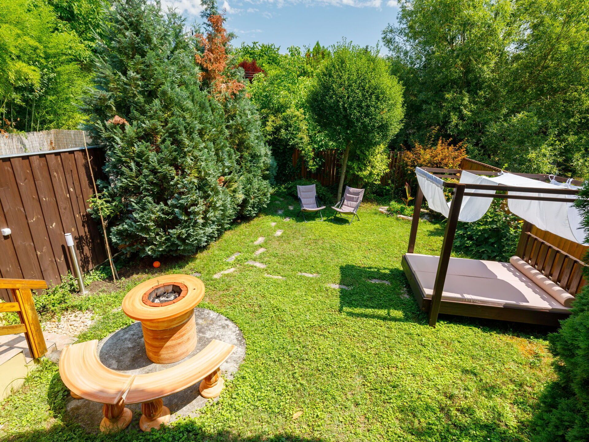 A backyard with a fire pit, two chairs, a wooden deck, and a pergola with a drying rack.