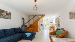 Una sala de estar con un sofá, una silla de mimbre, una chimenea y una escalera que conduce a una cocina y comedor.