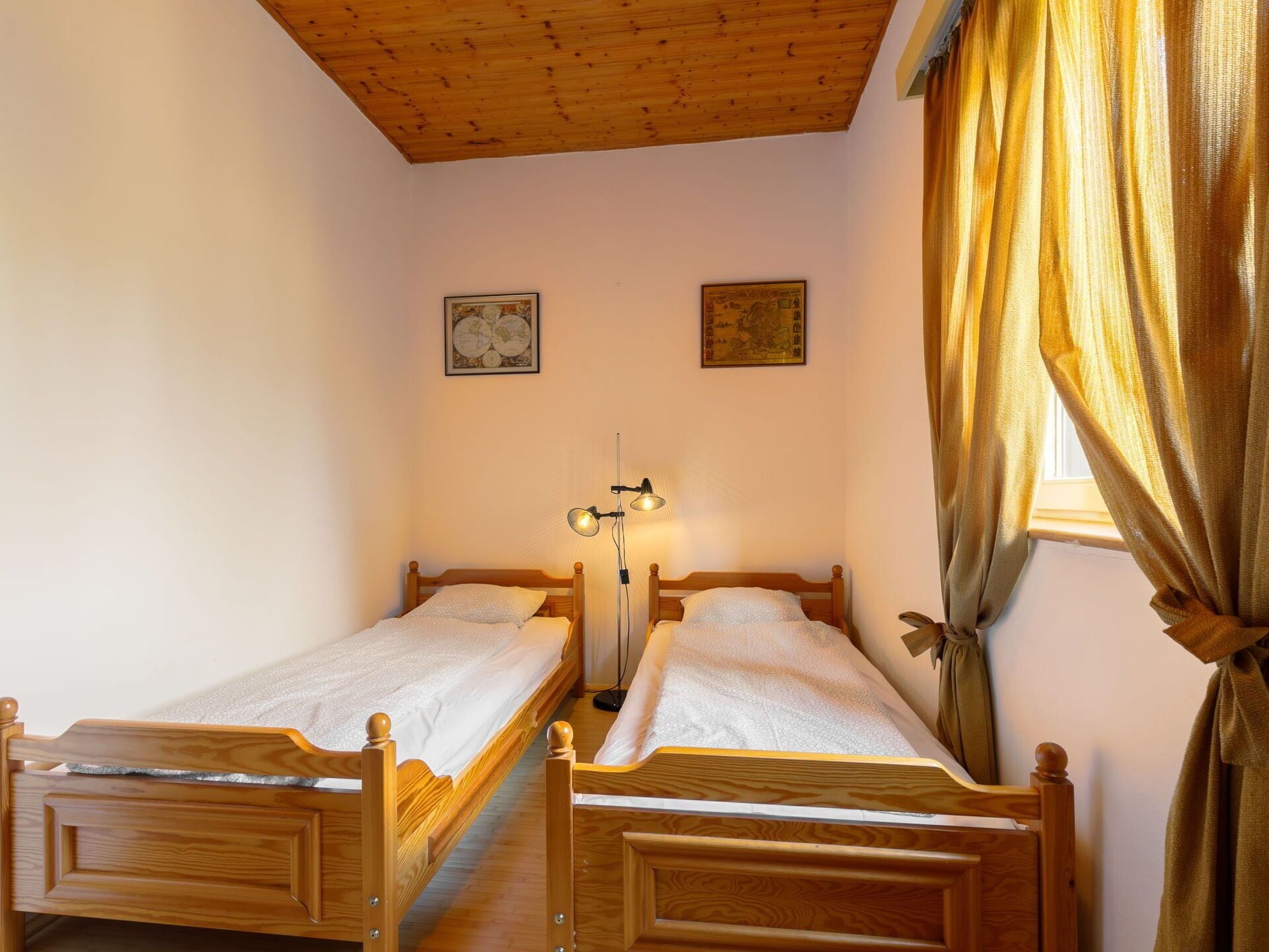 A room with two wooden beds, a wooden ceiling, and a window with curtains.