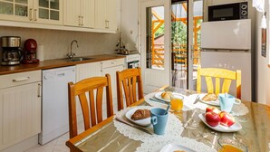 Una cocina con armarios blancos, microondas y refrigerador. Hay una mesa de comedor con sillas, una cafetera y un plato de comida.