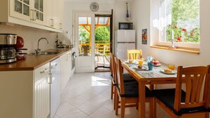 Una cocina con armarios blancos, una mesa de comedor con sillas, un refrigerador y una ventana con vistas a zonas verdes.