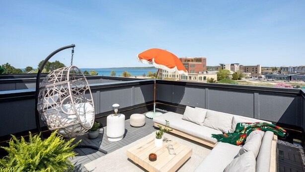 A rooftop terrace with a hanging chair, a cushioned sofa, and a wooden coffee table. - The Loft on Gillis | AC | Downtown | Beach | Rooftop | (Traverse City)
