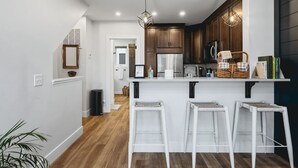 A modern kitchen with a central island, white bar stools, wooden cabinets, and pendant lighting. - The Loft on Gillis | AC | Downtown | Beach | Rooftop | (Traverse City)