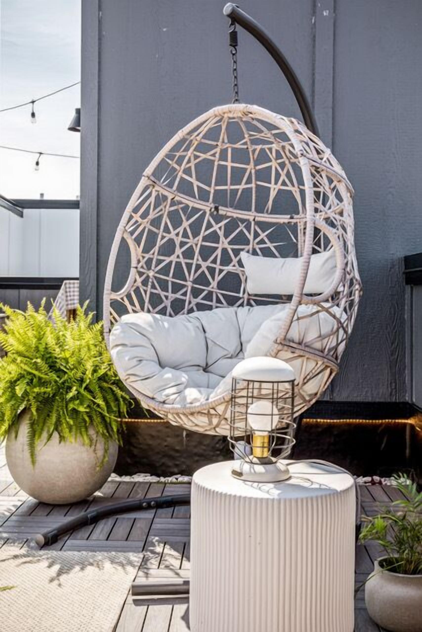 En hængeæggestol med pude, en potteplante og en bordlampe på en træterrasse.