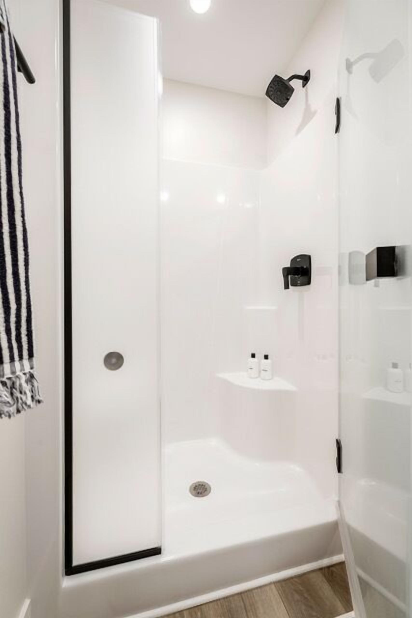 A modern bathroom with a glass-enclosed shower, a towel rack, and a shelf with toiletries.