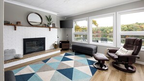 Un salon avec une cheminée, une grande fenêtre, un canapé et un fauteuil à bascule.