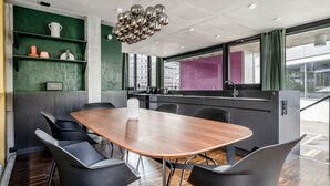 A modern kitchen with a wooden table and black chairs, a hanging light fixture, and a view of the city through large windows. - Clean Wiedikon 2BR w/ Storage & W/D, close to Market, by Blueground (Zurich)
