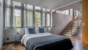 A modern bedroom with a large bed, a nightstand, a lamp, and a view of the outside through large windows. - Clean Wiedikon 2BR w/ Storage & W/D, close to Market, by Blueground (Zurich)