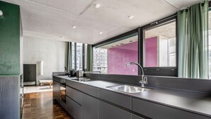A modern kitchen with a large island, stainless steel sink, and a view of the city through large windows. - Clean Wiedikon 2BR w/ Storage & W/D, close to Market, by Blueground (Zurich)