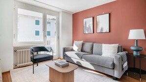 Een moderne woonkamer met een grijze bank, een zwarte stoel, een houten salontafel en een vloerlamp.