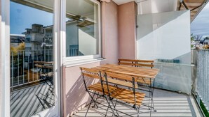 Een balkon met een tafel en stoelen, een glazen deur en uitzicht op gebouwen.