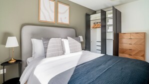 Een keurig opgemaakt slaapkamer met een bed, nachtlampjes, een kledingkast en een dressoir.