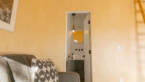 Une pièce comprenant un canapé, une porte donnant sur une cuisine et un miroir fixé au mur.