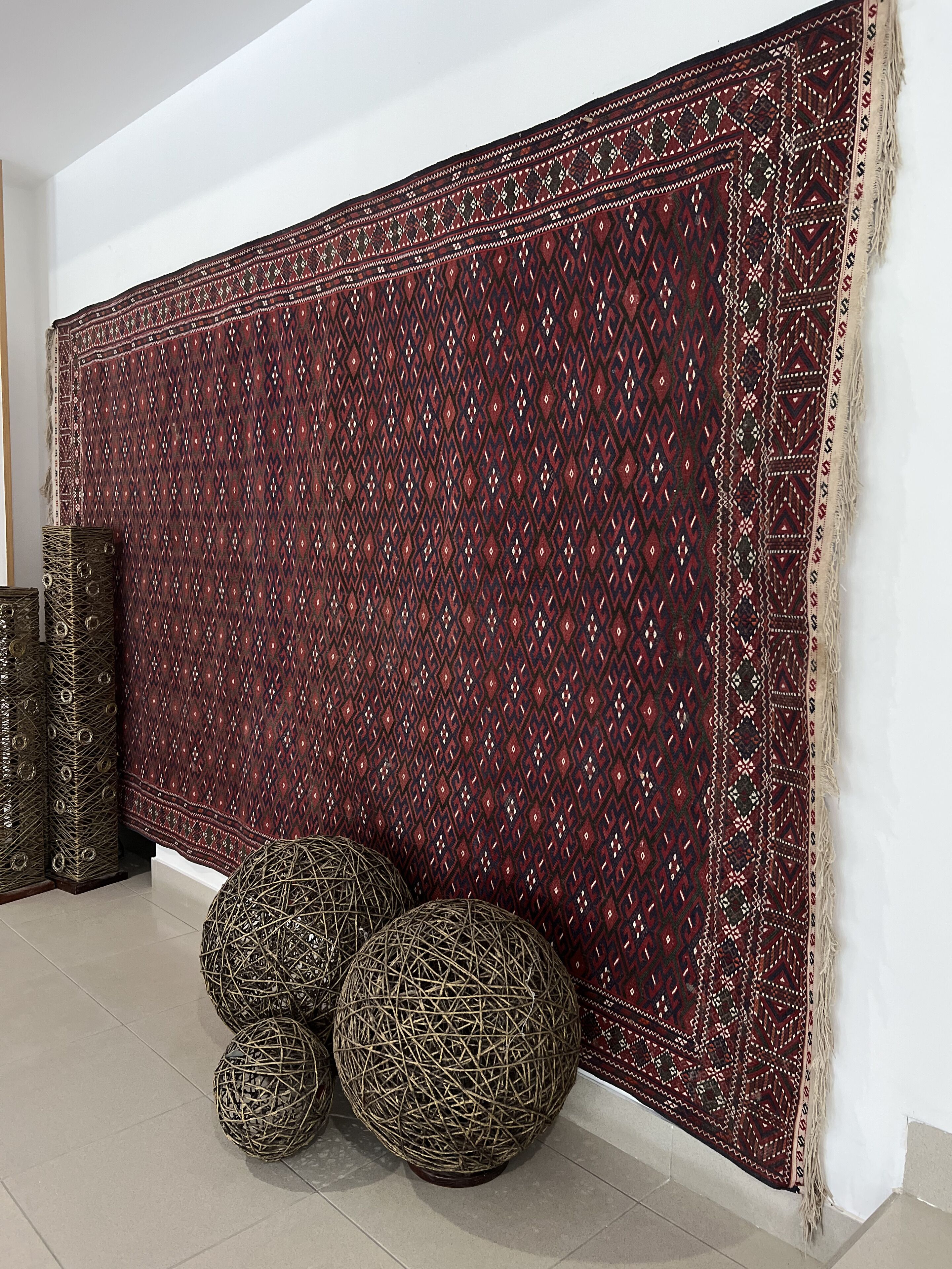 Una habitación con un tapete grande de estampado llamativo, esferas de mimbre y un armario alto de color oscuro.
