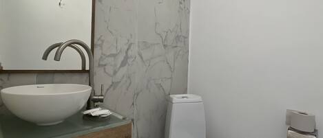 Ein Badezimmer mit Marmorfliesenspiegel, einem Holzbadezimmerschrank, einem weißen Waschbecken, einer Toilette und einem an der Wand montierten Toilettenpapierhalter.