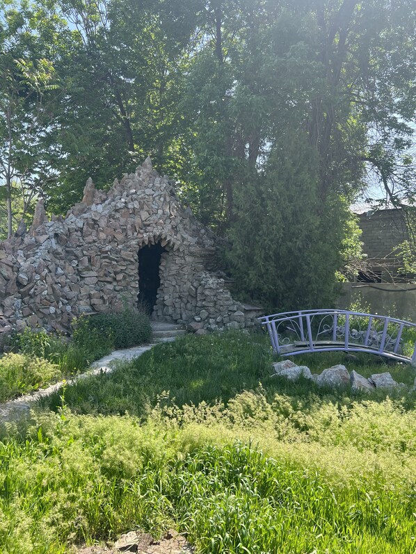 A stone structure with an entrance, surrounded by greenery and a metal bridge. - Tourist hotel (Shymkent)
